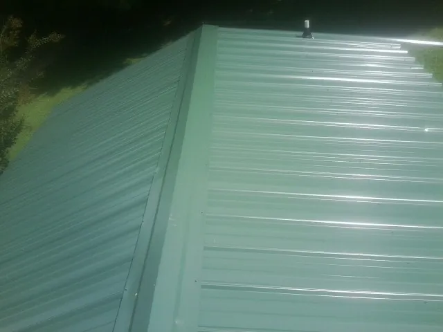 New green metal panels meeting at the ridge of a roof — Flat Roof Repair work by our crew in Oak Harbor
